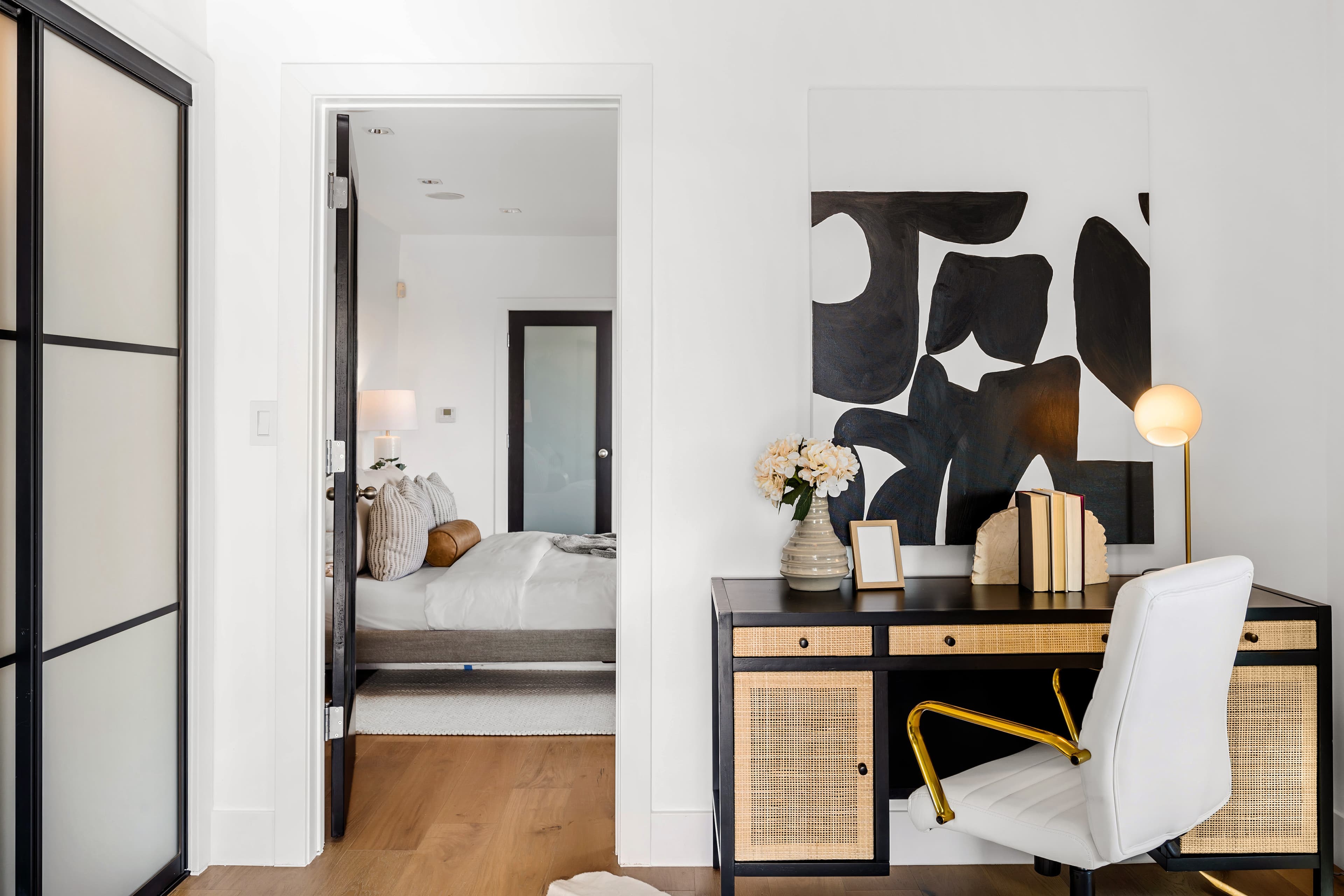 Interior design Sydney: home office nook with rattan desk and bold abstract artwork, opening onto a bedroom