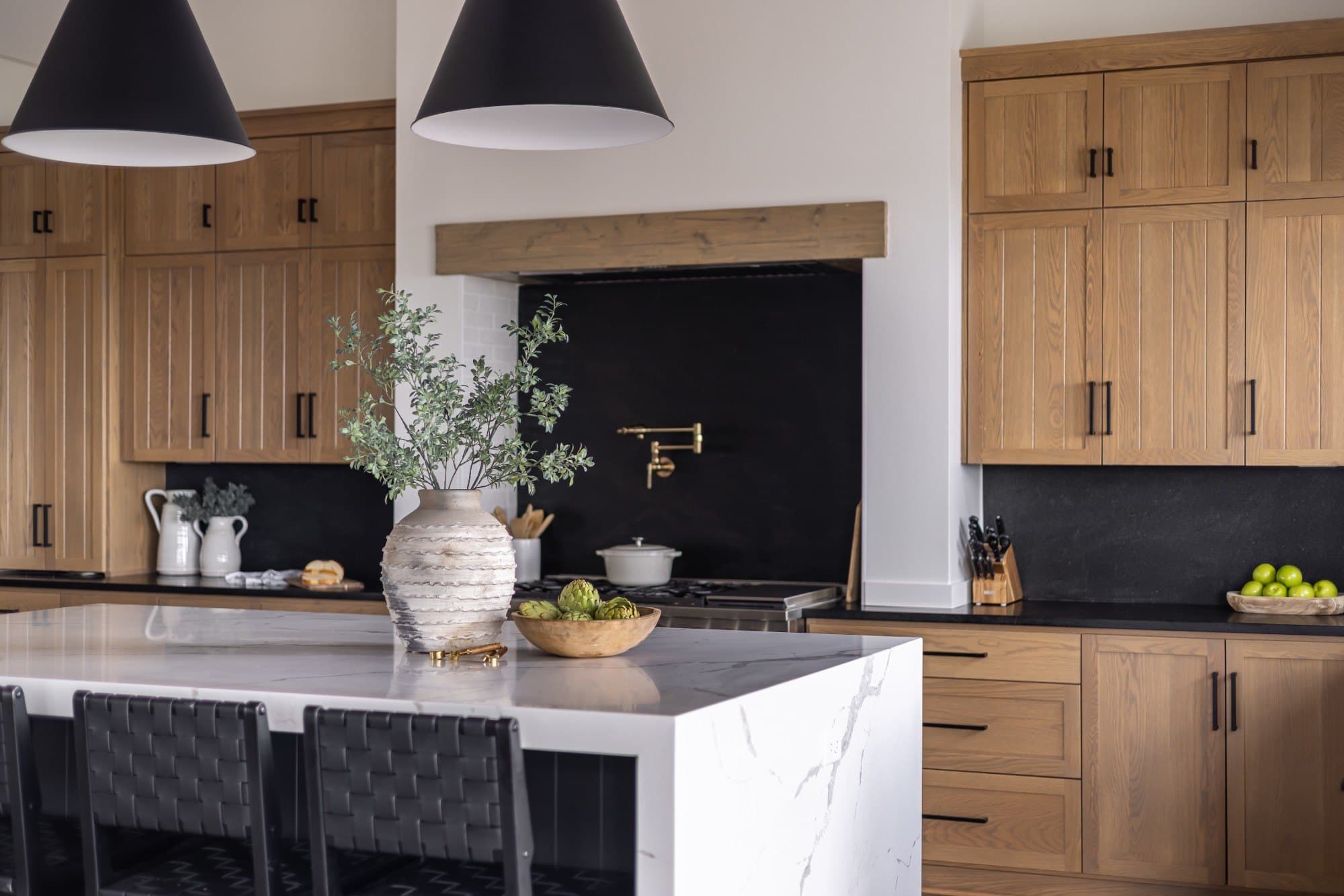 Interior design Sydney: kitchen with oak cabinetry, a black range nook with a brass pot filler, and a marble waterfall island